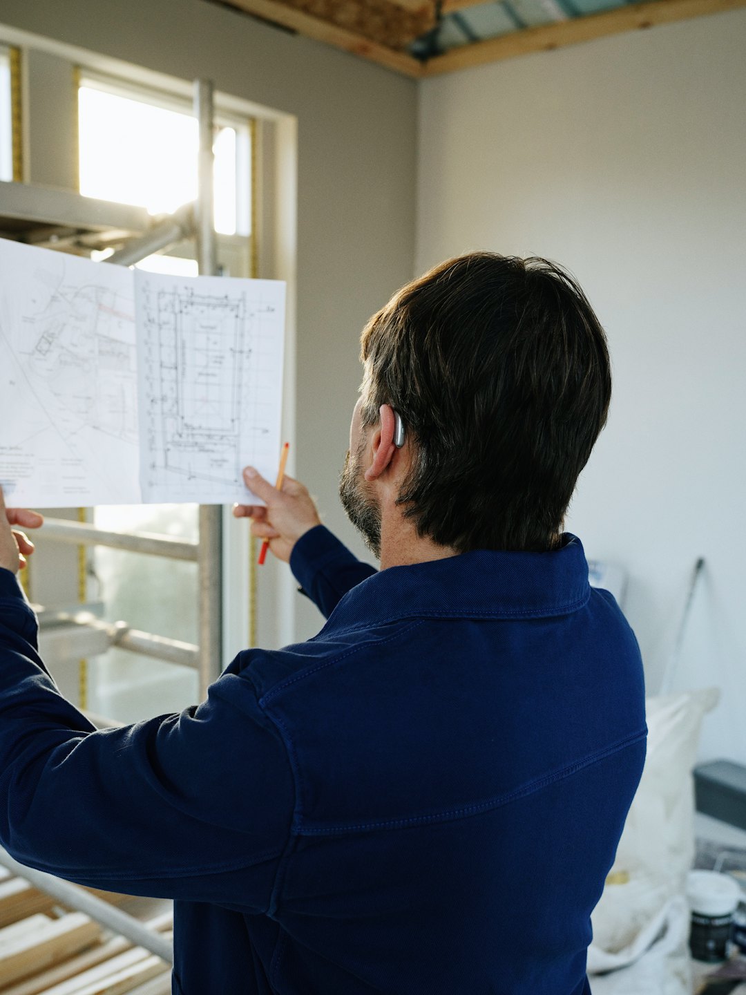Un ouvrier du bâtiment consulte des plans dans une pièce inachevée.