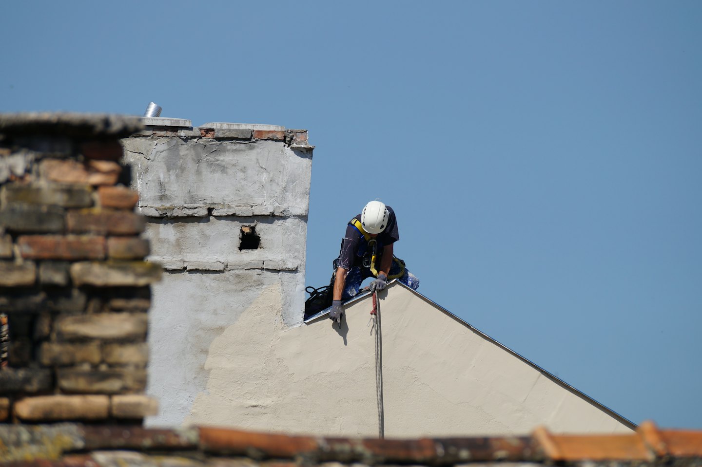 Un homme en casque de sécurité inspecte un toit à deux versants beige.