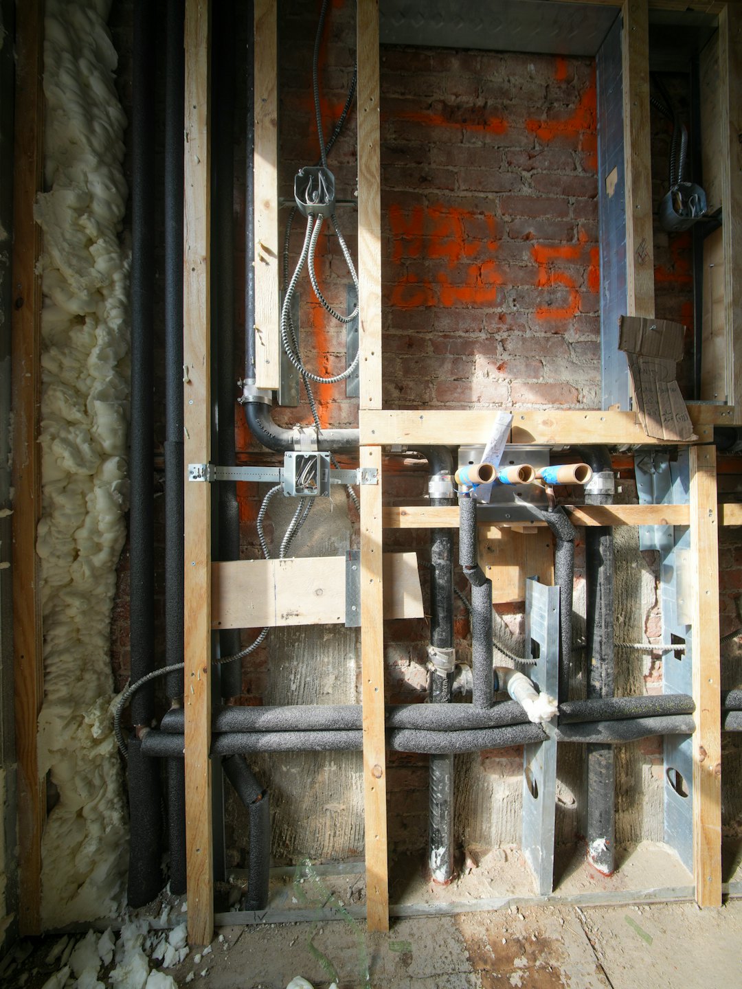 Rénovation de bâtiment montrant tuyaux, câblage et isolation sur mur de briques.